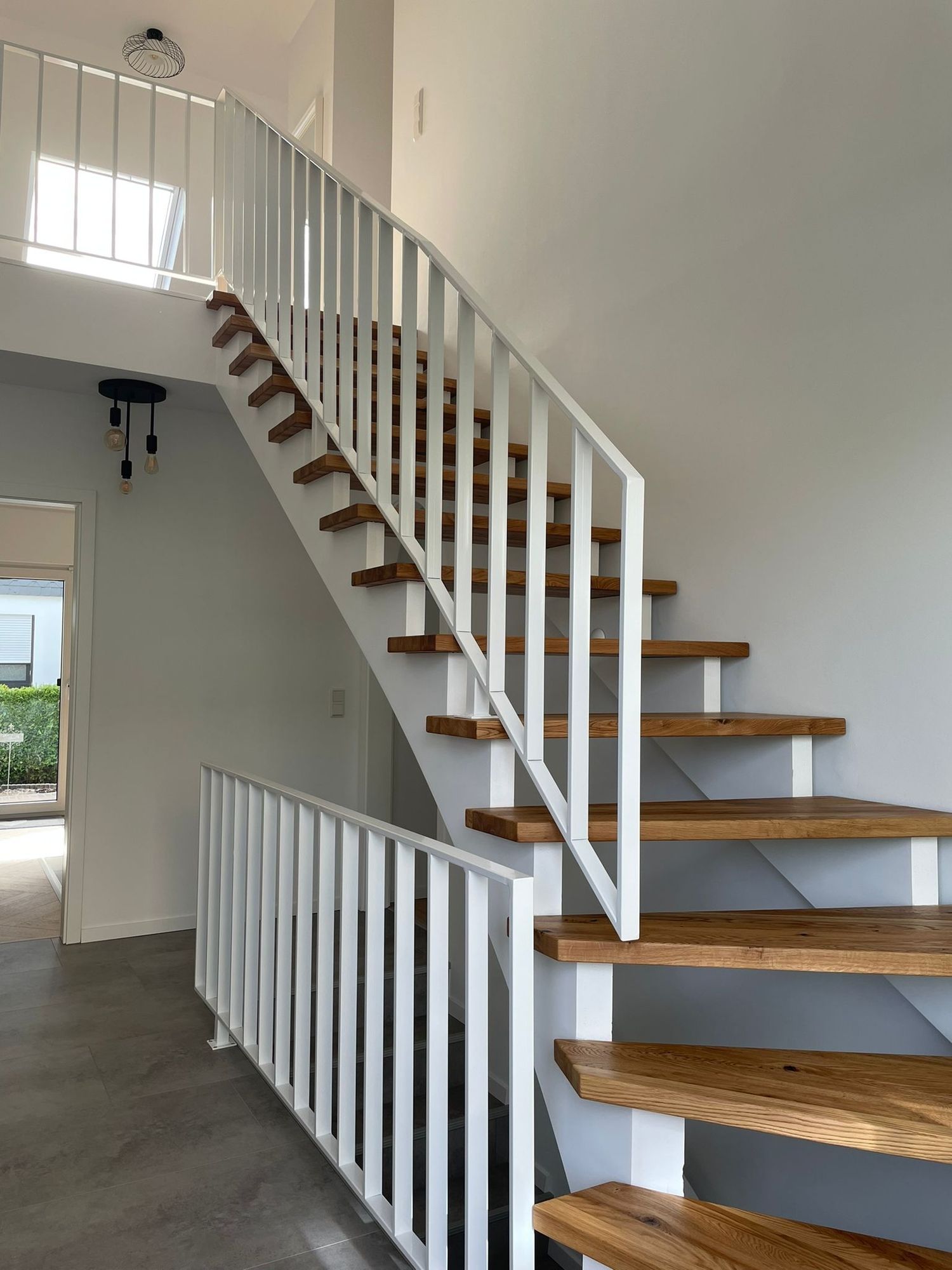 Eine moderne Treppe mit Holzstufen und weißem Geländer in einem hellen Treppenhaus mit großem Fenster